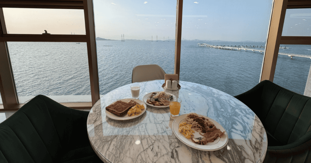 Breakfast buffet table at Wave M Hotel West restaurant, appearing to float above the ocean with panoramic West Sea views.