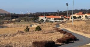 Clubhouse and fairway view at Adenhill CC Jeju with wind turbines in the distance, highlighting the rolling terrain influenced by the Mount Halla effect.