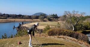 제주 아덴힐CC 티잉 구역에서 한라산을 배경으로 아이언 샷을 준비하는 골퍼와 워터 해저드 전경
