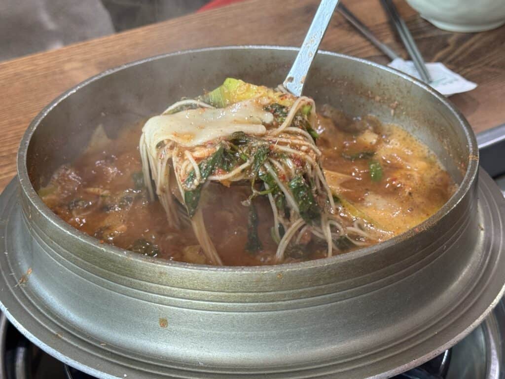 한국 전통 음식인 김치찌개와 신선한 재료가 어우러진 모습입니다.